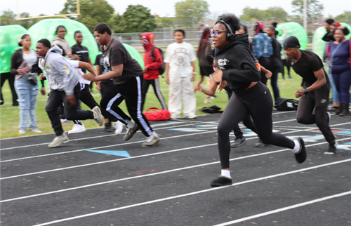  A girl and boy running on a track. Students stand and watch.